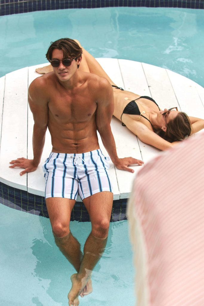 Style plage homme : le guide pour être stylé cet été 2 Short de bain homme blanc à rayures, coupe mi-cuisse pour un style plage soigné
